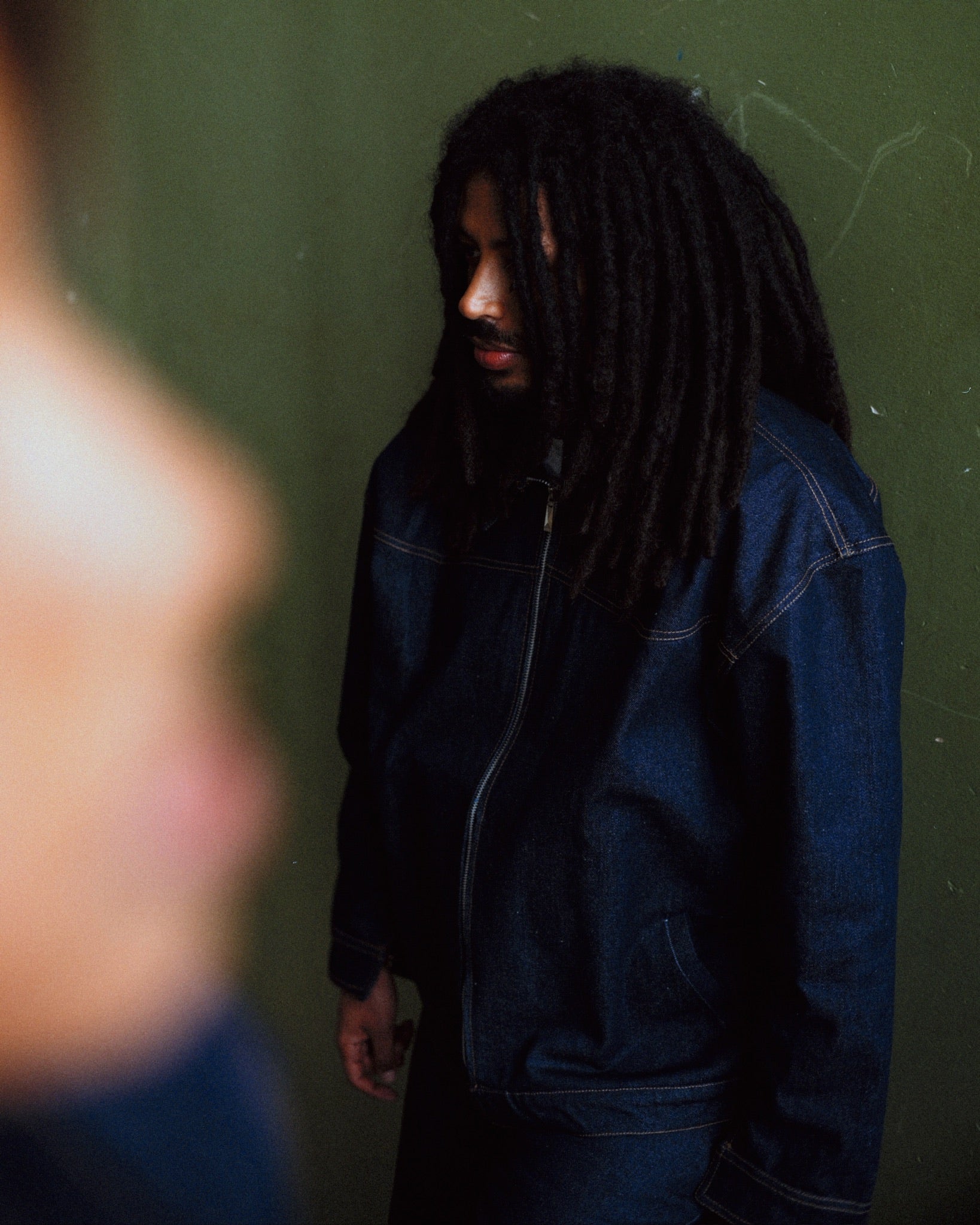 no véx denim jacket and jeans worn, green wall